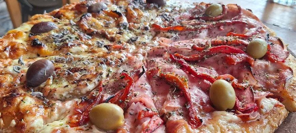 Pizza al molde con jamón, morrones asados y aceitunas, recién salida del horno de barro