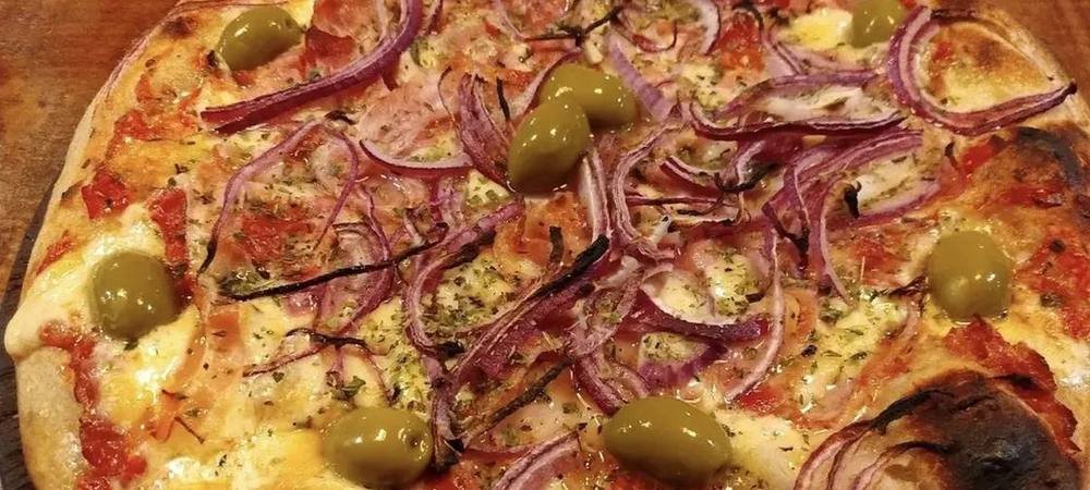 Pizza con cebolla morada, tomate y aceitunas verdes sobre tabla de madera