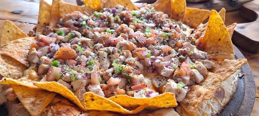 Pizza cubierta de nachos y pollo con verduras picadas